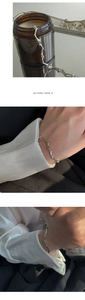 Gros plan d'un bracelet en métal liquide argenté irrégulier sur le poignet au design minimaliste