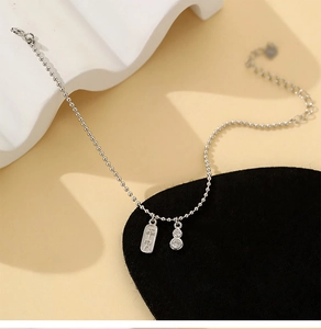 Détail du bracelet en perles argentées avec plaque Pingan et breloque gourde sertie