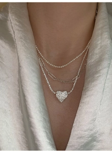 Close-up of layered necklace set featuring a sparkling heart pendant and freshwater pearls