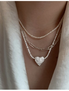 Detailed view of triple-layered necklaces with textured heart pendant and pearls