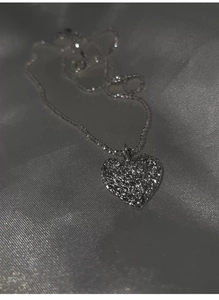 Macro shot of a silver heart pendant with hammered lava texture on grey silk fabric