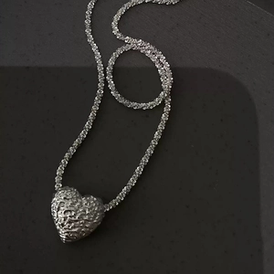 Textured lava heart pendant necklace with fine stardust chain on black matte background