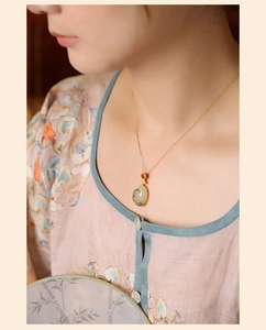 Detailed close-up of a Hetian jade pendant necklace with gold floral metalwork on a model