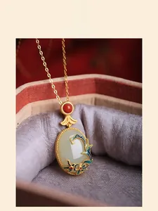 Macro shot of gold-plated white jade pendant with blue enamel wave pattern and red gemstone