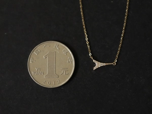 Detailed close-up of golden geometric V-pendant with sparkling crystals and coin for scale