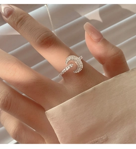 Close-up of silver crescent moon ring with zircon stones worn on finger with soft shadows