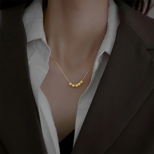 Détail du collier à billes dorées avec cinq charmes rotatifs sur une chaîne fine