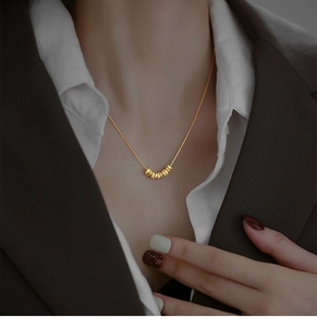 Détail d'un collier doré à perles porté avec une chemise blanche et un blazer