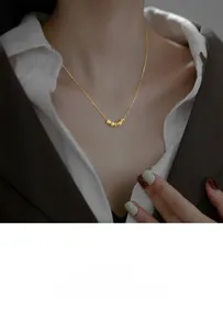 Détail de cinq perles dorées sur une chaîne portée avec une chemise et un blazer