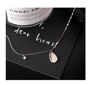 Macro detail of silver teardrop necklace with engraved text and zircon on black surface