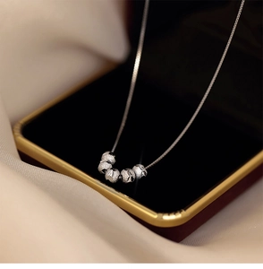 Détail de cinq perles argentées mates sur chaîne fine posée sur un écrin à bijoux