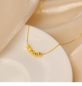 Gros plan d'un collier doré avec des perles mates sur céramique blanche et satin