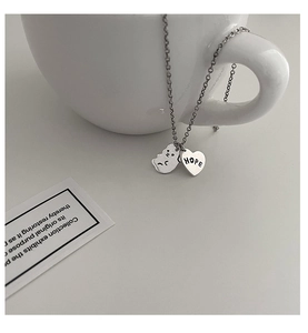 Détail du collier argenté avec cœur gravé HOPE et pendentif en forme de visage