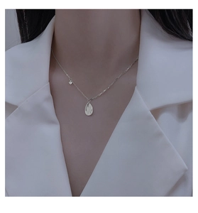 Detail of asymmetrical silver necklace with zircon pendant and engraved oval tag on model