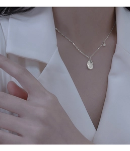 Detail of silver drop necklace with zircon and oval engraved tag worn by model