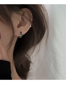 Gros plan d'une boucle d'oreille croix noire et d'un faux piercing argenté sur l'oreille