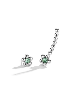Détail de puce fleur asymétrique et boucle d'oreille grimpante aux pierres vertes