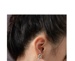 Gros plan d'une boucle d'oreille fleur argentée avec pierre verte sur l'oreille