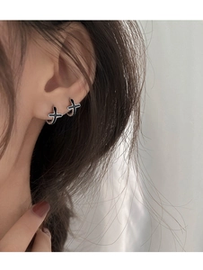 Gros plan de boucles d'oreilles créoles noires en forme de croix sur l'oreille