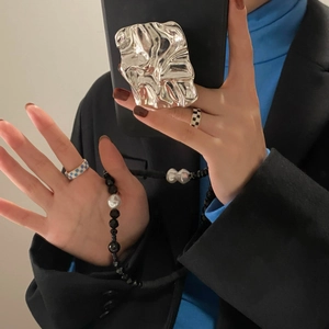 Detail showing checkered open rings and silver textured phone accessory on a model