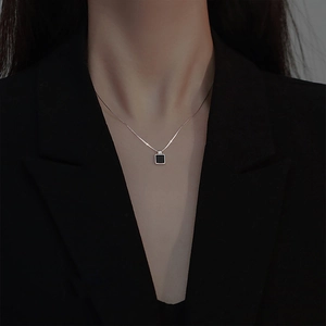 Gros plan d'un collier pendentif carré noir porté par un mannequin en veste noire