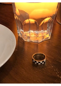 Close-up of checkerboard enamel ring placed on a rustic wooden table in warm lighting