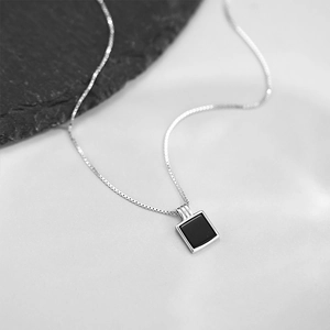 Gros plan d'une chaîne argentée avec pendentif carré noir sur un fond de pierre