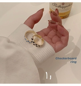 Close-up of stylish black and blue checkerboard enamel open rings worn over a white sweater