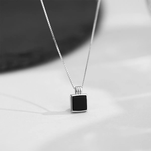 Détail d'une chaîne vénitienne argentée avec un pendentif carré noir minimaliste