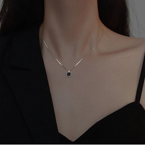 Gros plan d'un collier minimaliste avec pendentif noir carré sur chaîne argentée porté par un mannequin