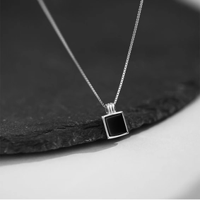Gros plan d'un pendentif carré en argent minimaliste avec onyx noir sur une pierre sombre