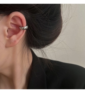 Macro shot of minimalist silver ear cuff on ear with high-polish metallic finish