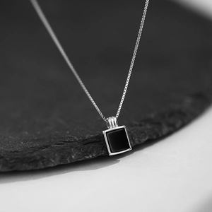 Élégant collier boîte en argent avec pendentif carré en onyx noir sur fond de pierre noire