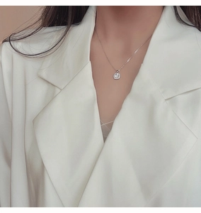 Dettaglio della collana con pendente quadrato e micro-pavé di cristalli su blazer bianco