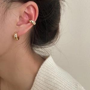 Close-up of polished gold ear cuffs and chunky hoop earrings worn on a female model
