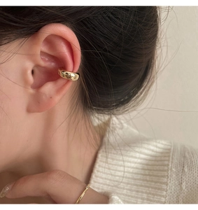 Close-up of elegant gold ear bone clip and minimalist ring on a woman wearing a sweater