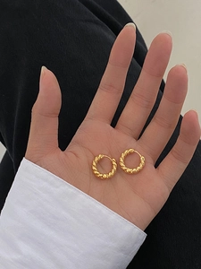 Macro detail of golden twisted rope hoop earrings held in hand for size perspective