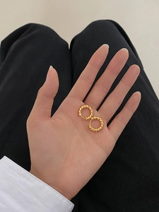 Close-up of golden twisted hoop earrings featuring a minimalist rope design on the palm
