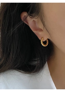 Detailed view of a twisted rope gold hoop earring worn on an earlobe with sharp metal texture
