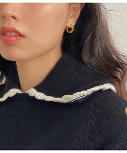Close-up of golden twisted rope hoop earrings worn by a model in a minimalist style