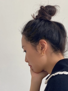 Close-up of model wearing small golden twisted hoop earrings with a textured rope design