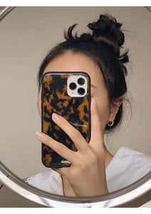 Close-up of twisted gold hoop earrings paired with a tortoiseshell pattern iPhone case
