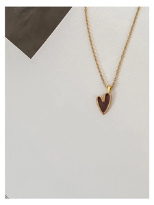 Nahaufnahme der minimalistischen Goldkette mit glänzendem weinrotem Herzanhänger
