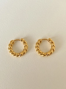 Detailed view of gold twist hoop earrings with a textured woven design on a light surface