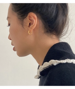 Close-up of a female model wearing gold twisted hoop earrings with a polished finish