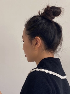 Detail of gold twisted rope hoop earrings shown on a model with minimalist black knit sweater