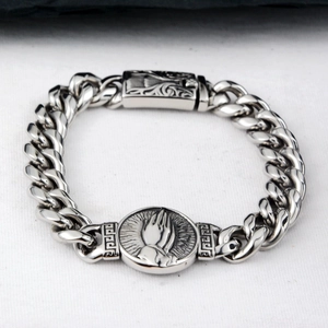 Detail of silver Cuban chain bracelet with Praying Hands medallion and greek key accents