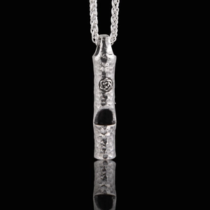 Macro shot of vintage hammer-textured silver whistle pendant with Celtic knot carving detail