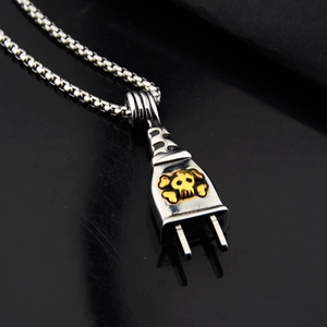 Macro shot of a silver punk plug pendant with a golden skull emblem on a box chain
