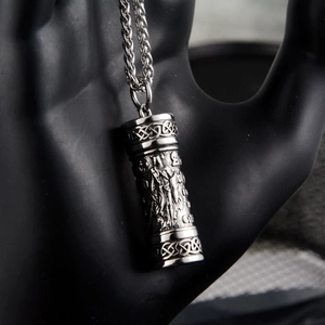 Macro detail of silver cylinder pendant with Nordic engravings on black hand model